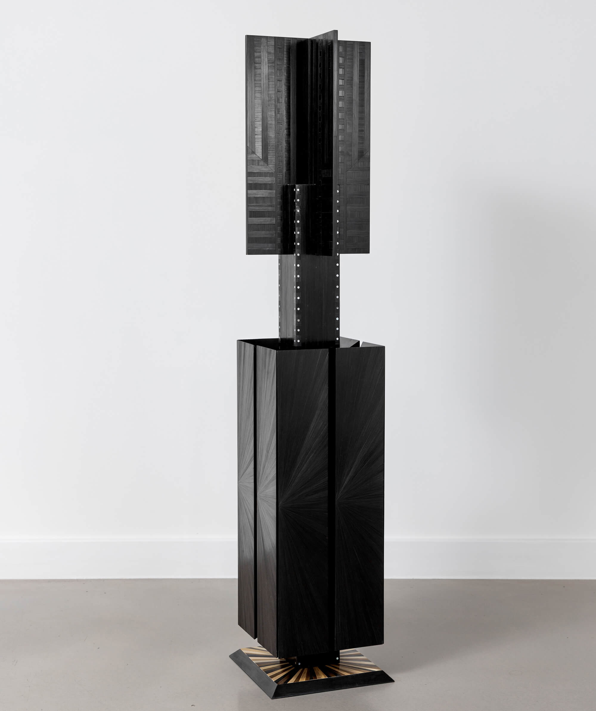 Black geometric sculptural object with textured surface standing on the floor