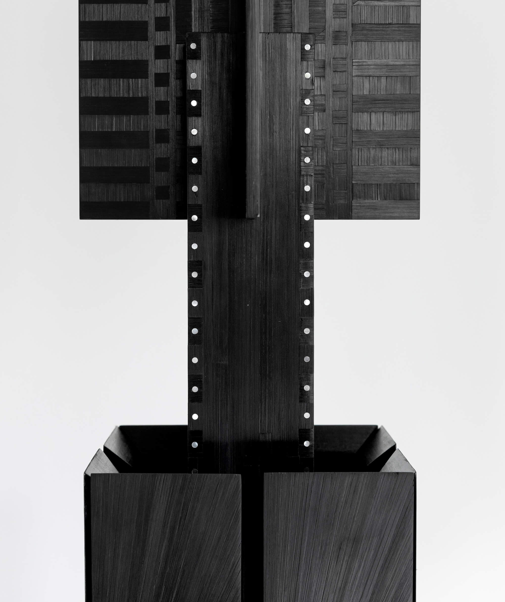 Close up of a black sculptural object with woven texture and white pearl details