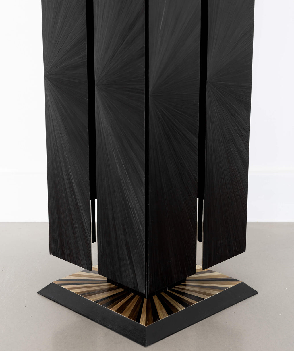 Close up of a black cuboid sculptural object standing on the floor with a sunburst patterned base