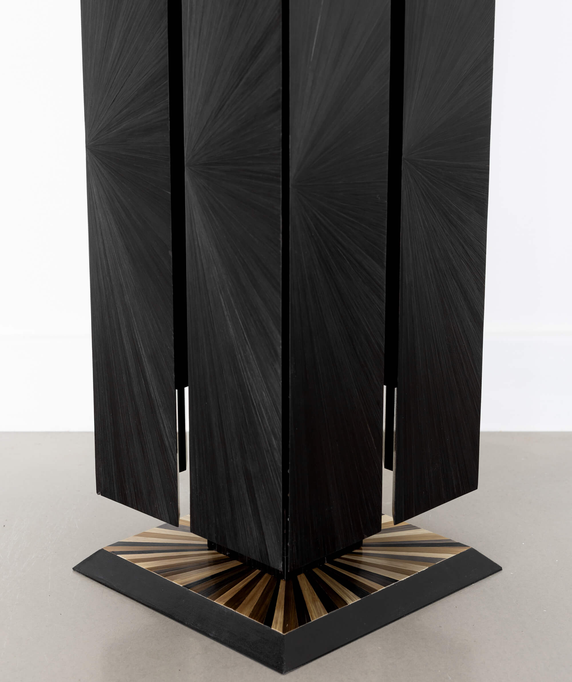 Close up of a black cuboid sculptural object standing on the floor with a sunburst patterned base