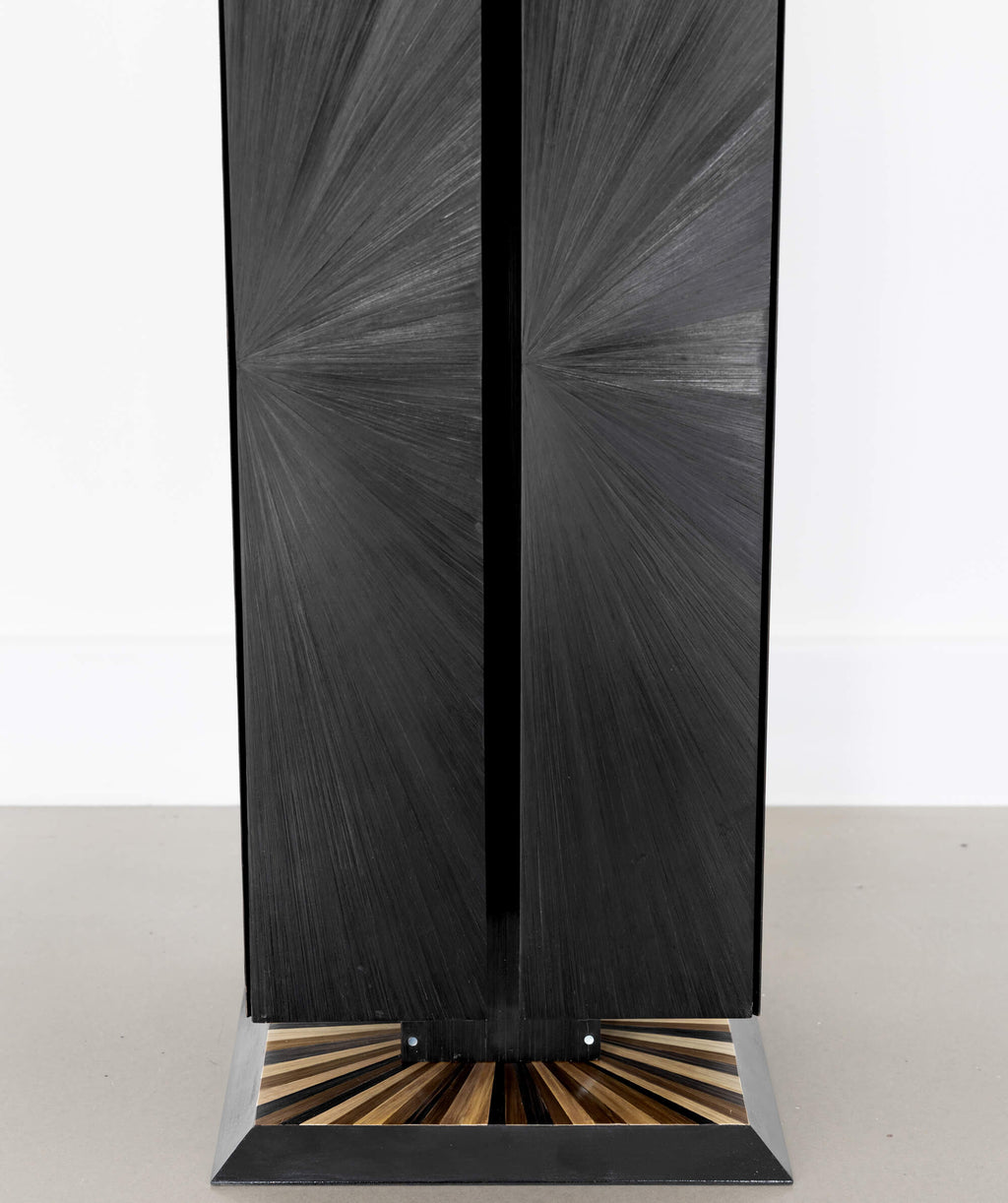Close up view of a black cuboid sculptural object with a sunburst patterned base