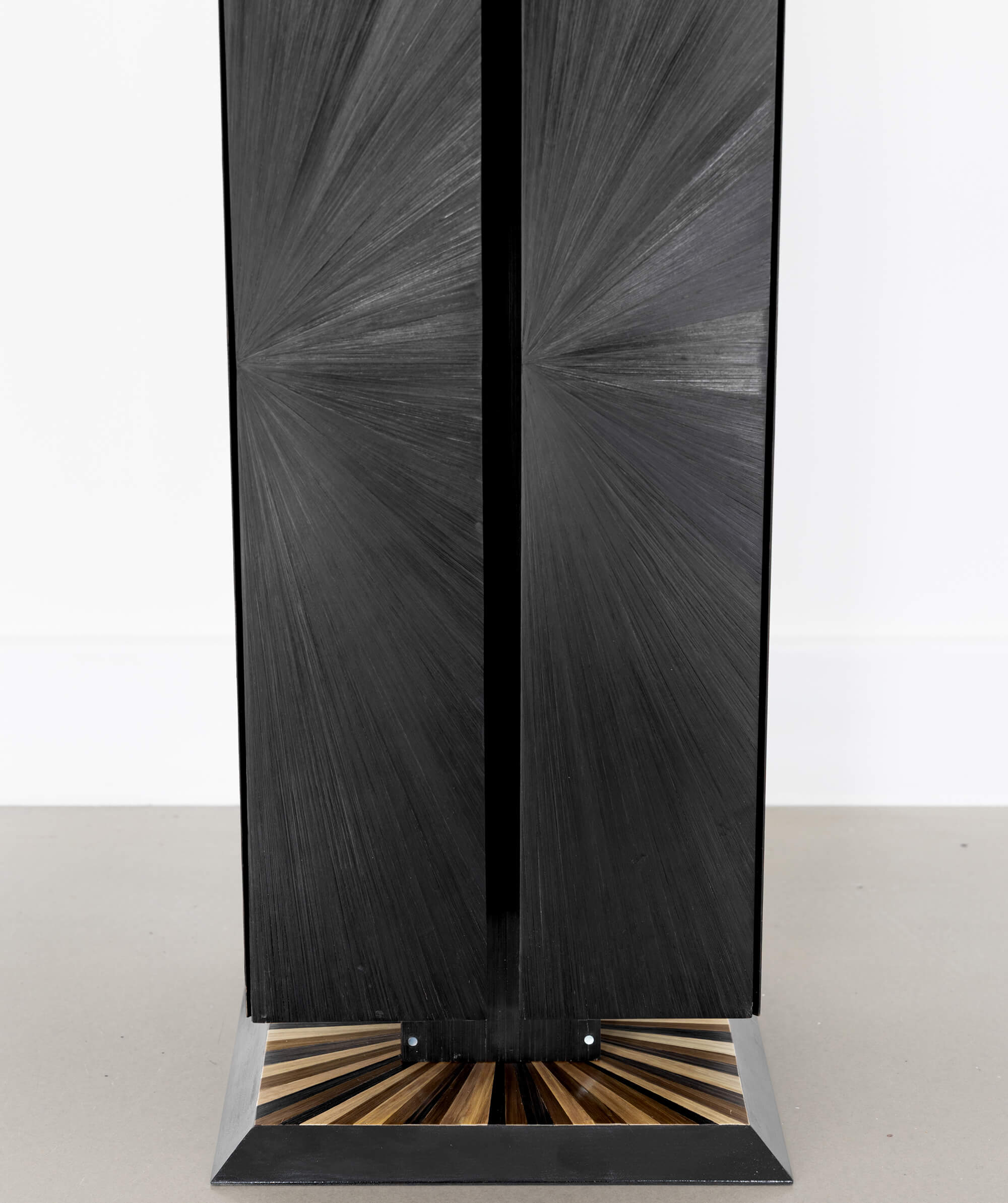 Close up view of a black cuboid sculptural object with a sunburst patterned base