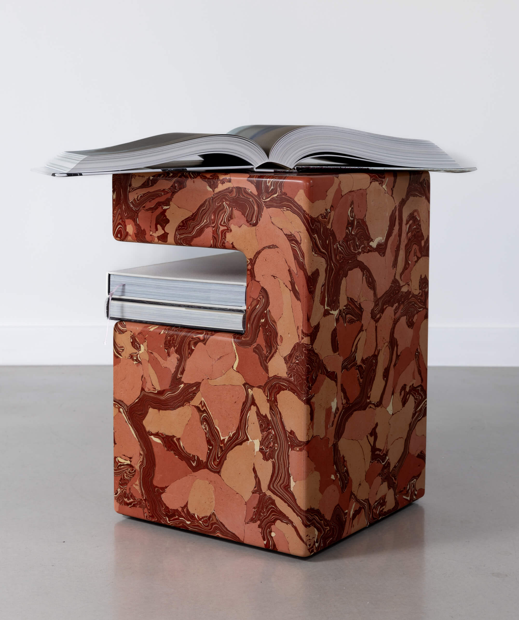 Side view of a marble patterned rectangular sculpture with coffee table books on a shelf and on the top