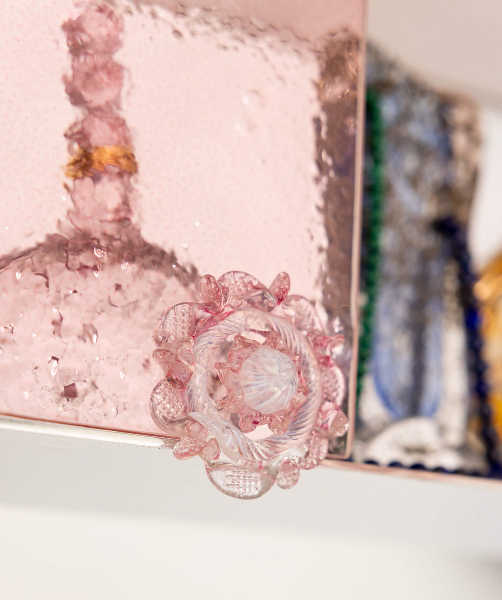 Close up of an ornate cabinet handle in pink glass on a pink glass door